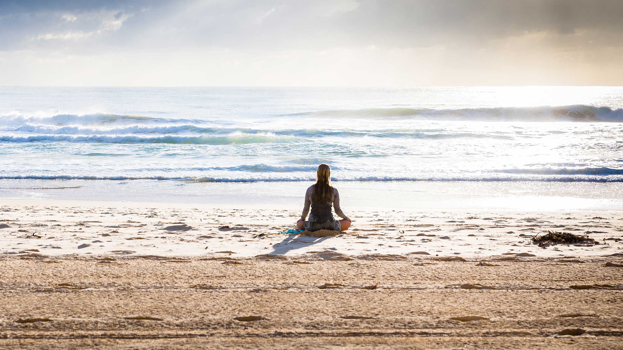 Femme méditant sur une plage face à l'océan
